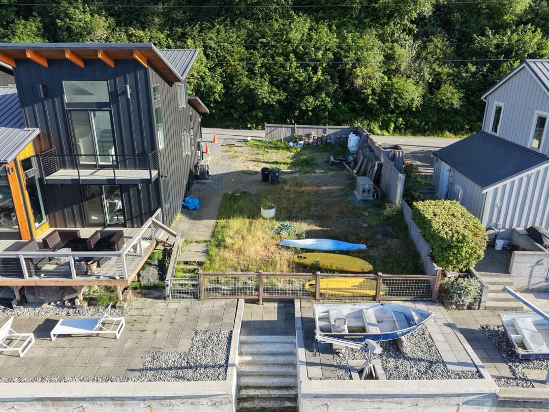 The waterfront yard before construction, with lawn and an existing path between the homes